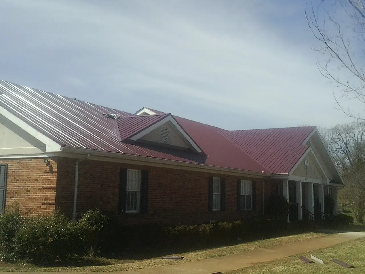 Red metal roof with gabled entries on a long brick building, from a Hail Damage Roof Repair job in Wentworth